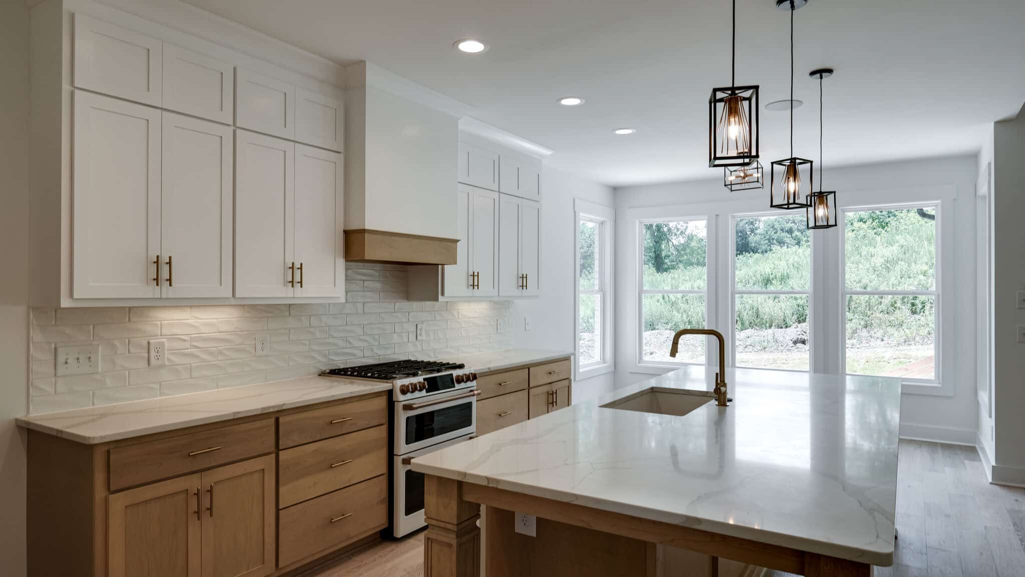 Modern kitchen with white cabinets, marble countertop, island, and pendant lights near large windows.