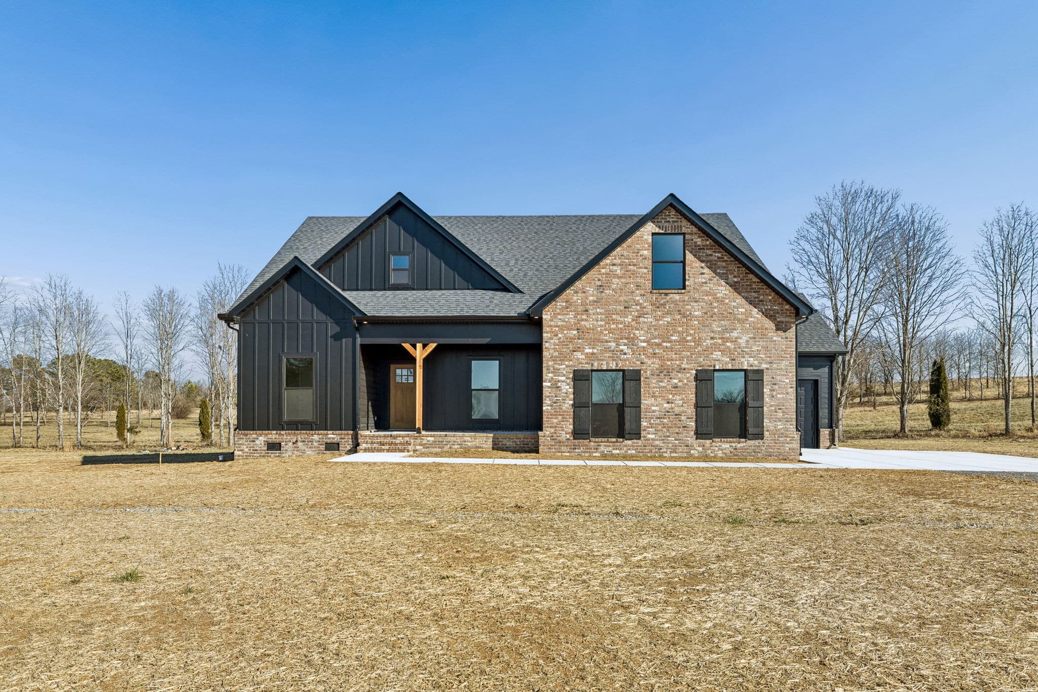 Modern farmhouse with brick and black exterior, front yard and clear blue sky.