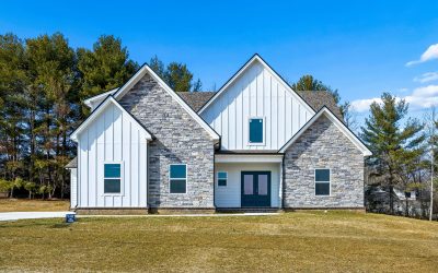 Modern farmhouse with stone and siding exterior, surrounded by trees under a clear blue sky.