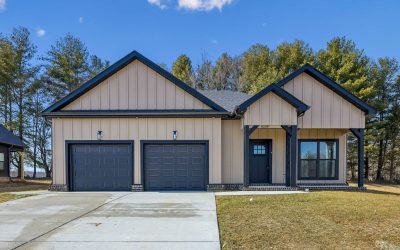 Modern farmhouse exterior with beige board-and-batten siding, black trim, two-car garage, driveway, and lawn