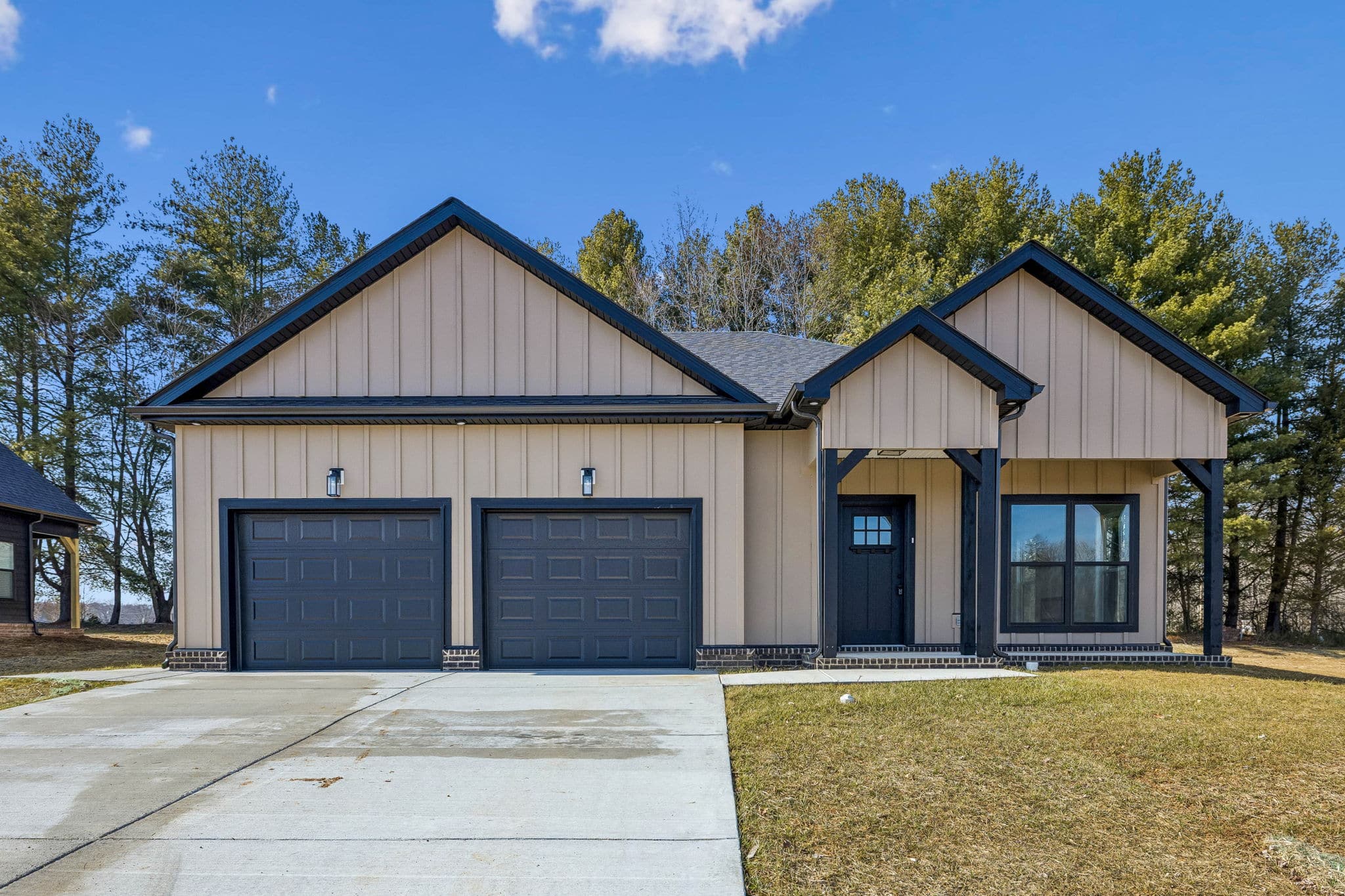 Modern farmhouse exterior with beige board-and-batten siding, black trim, two-car garage, driveway, and lawn