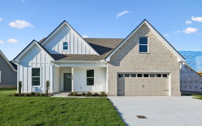 Modern suburban house with white siding, brick facade, two-car garage, and green lawn under blue sky.