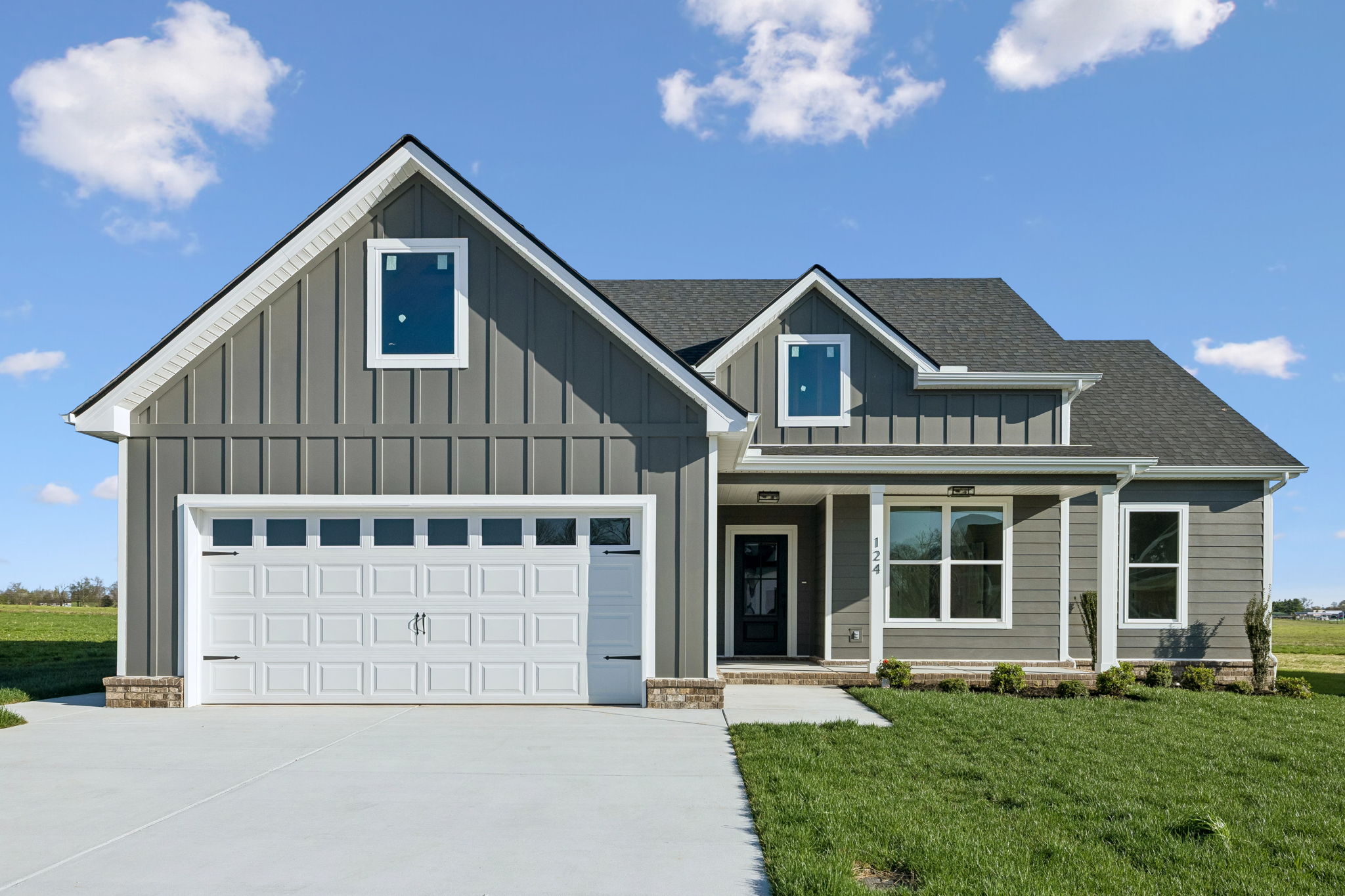 Modern gray house with white garage door, green lawn, and blue sky background.