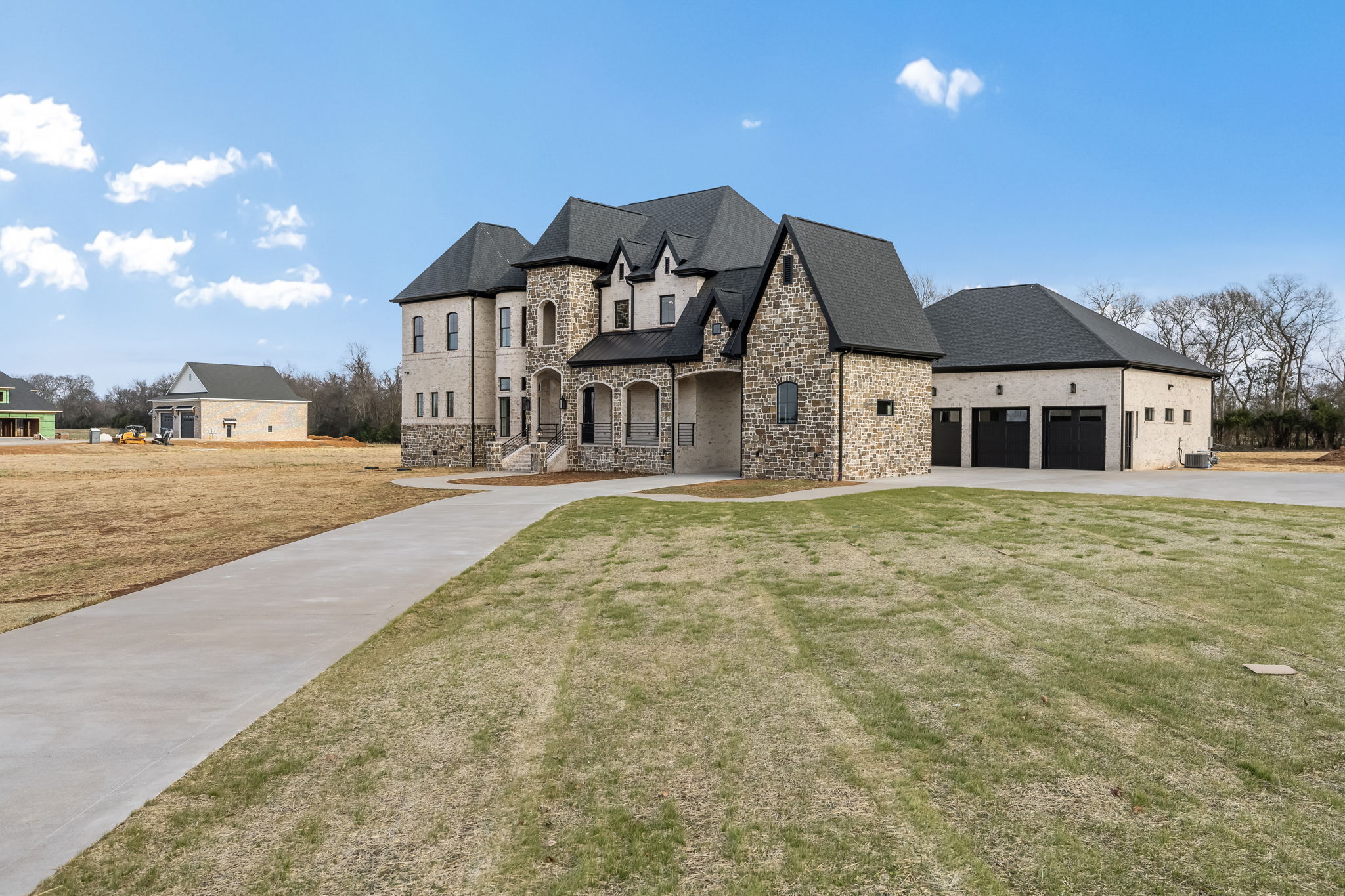 Large stone house with black roof, surrounded by grassy yard and clear blue sky.