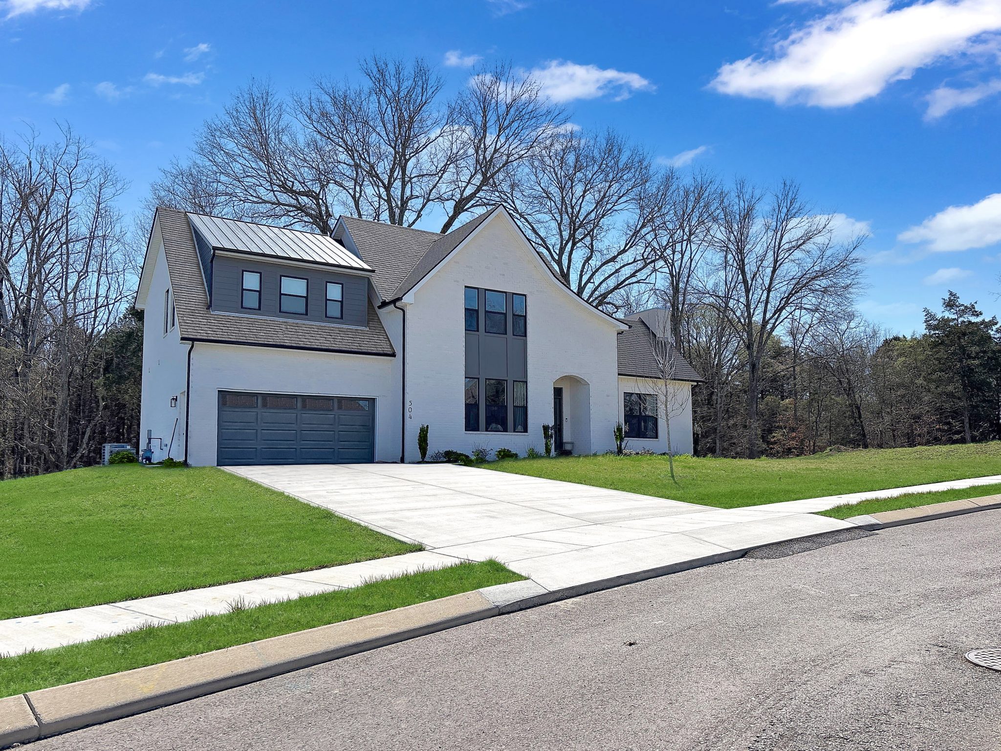Modern white house with large windows, two-car garage, and green lawn under a blue sky.