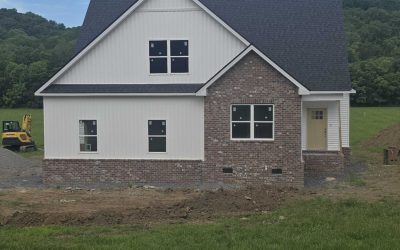 Newly built house with brick and siding exterior against a backdrop of lush green hills.