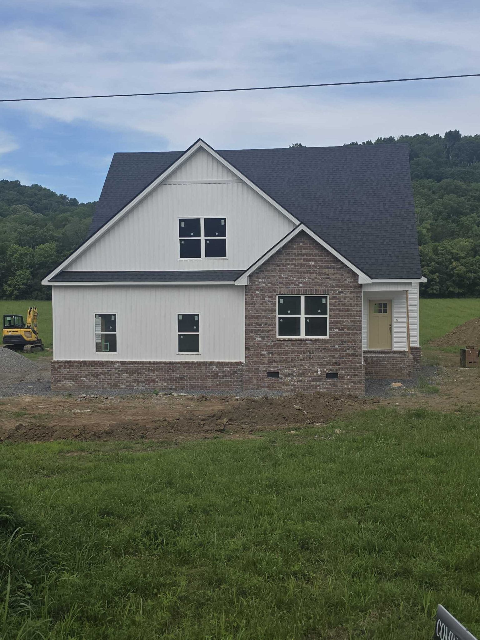 Newly built house with brick and siding exterior against a backdrop of lush green hills.