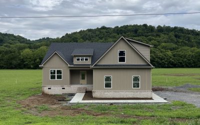 Newly built house in a grassy field with hills in the background under a cloudy sky.