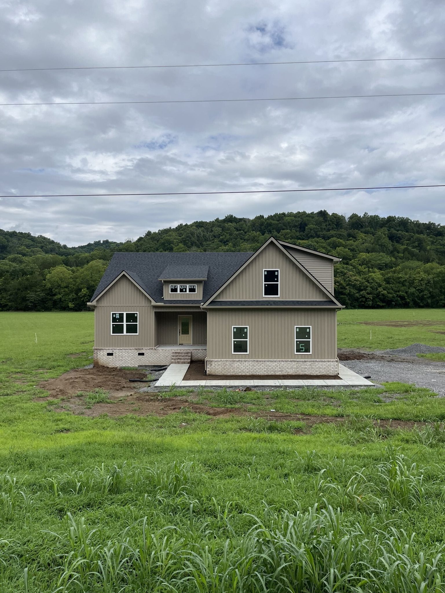 Newly built house in a grassy field with hills in the background under a cloudy sky.