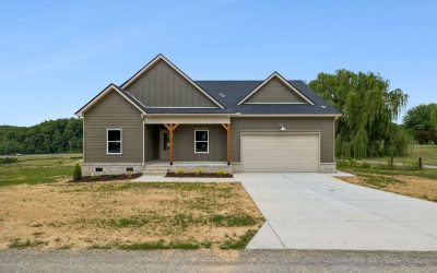Modern single-story house with gray siding and attached garage, set in a rural landscape.