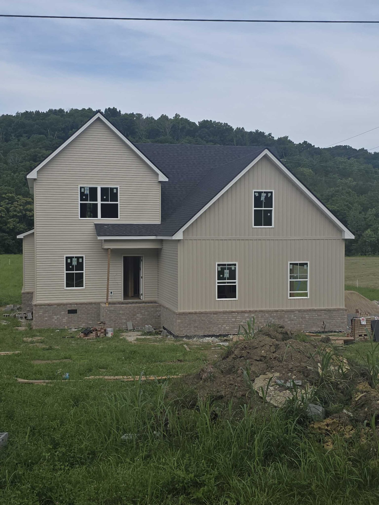 Two-story house under construction on a grass-covered lot, surrounded by trees.