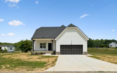 Modern farmhouse with black roof and garage, surrounded by grass, under a clear blue sky.