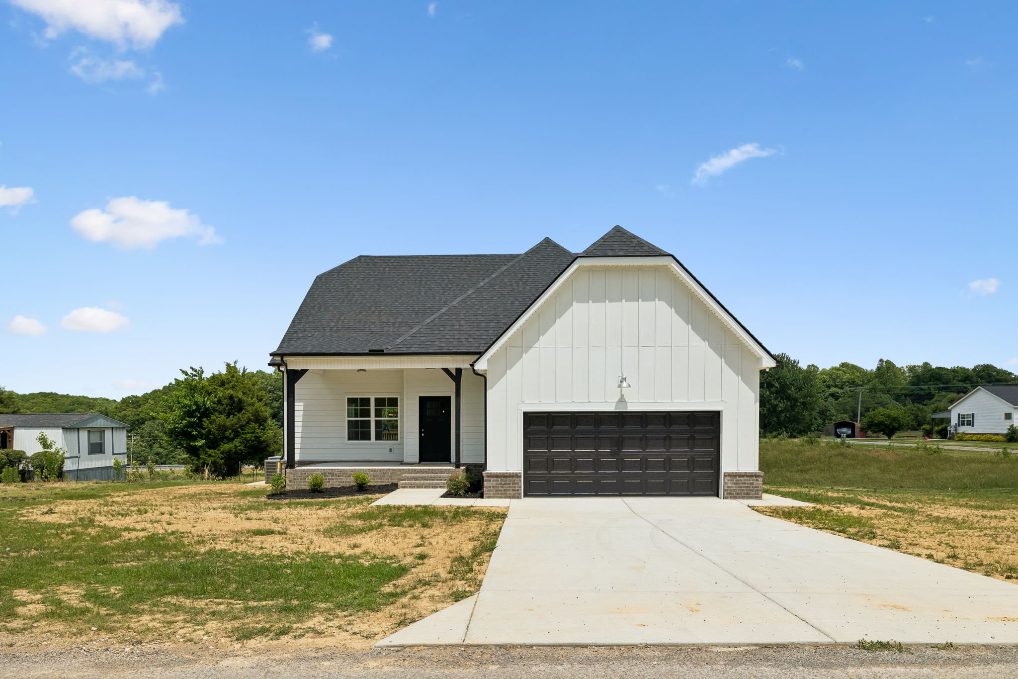 Modern farmhouse with black roof and garage, surrounded by grass, under a clear blue sky.