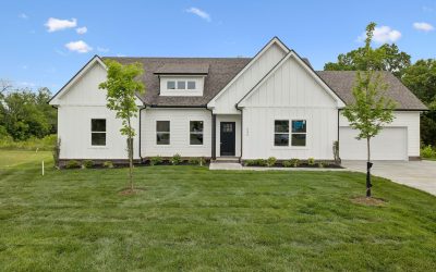 Modern white house with manicured lawn and trees under a clear blue sky.