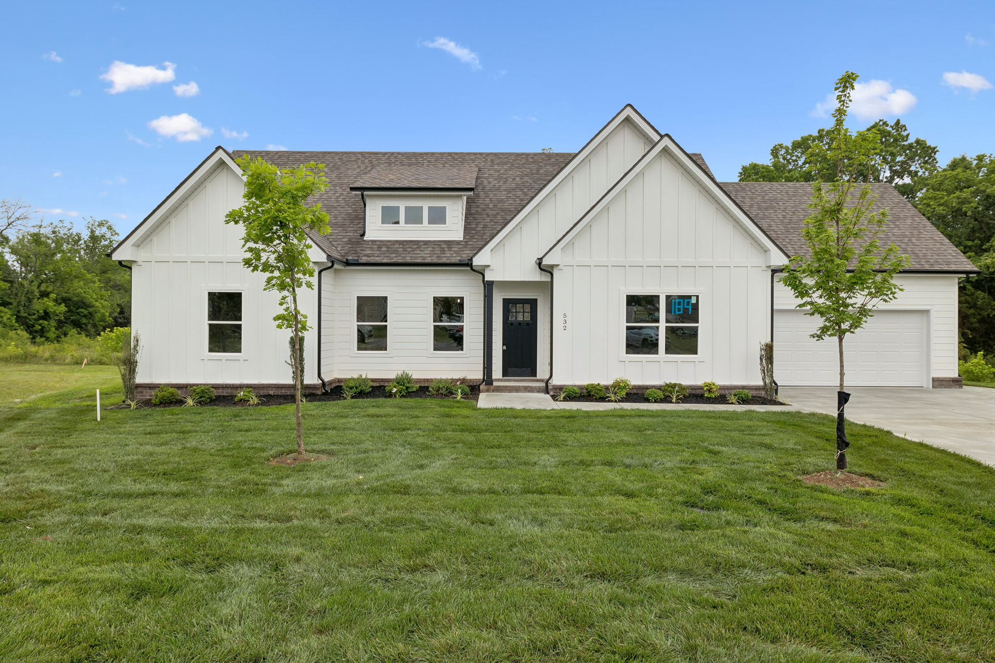 Modern white house with manicured lawn and trees under a clear blue sky.