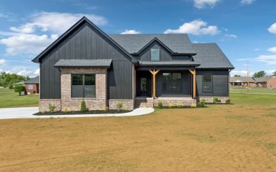 Modern black and brick house with gable roof in suburban setting, clear blue sky.