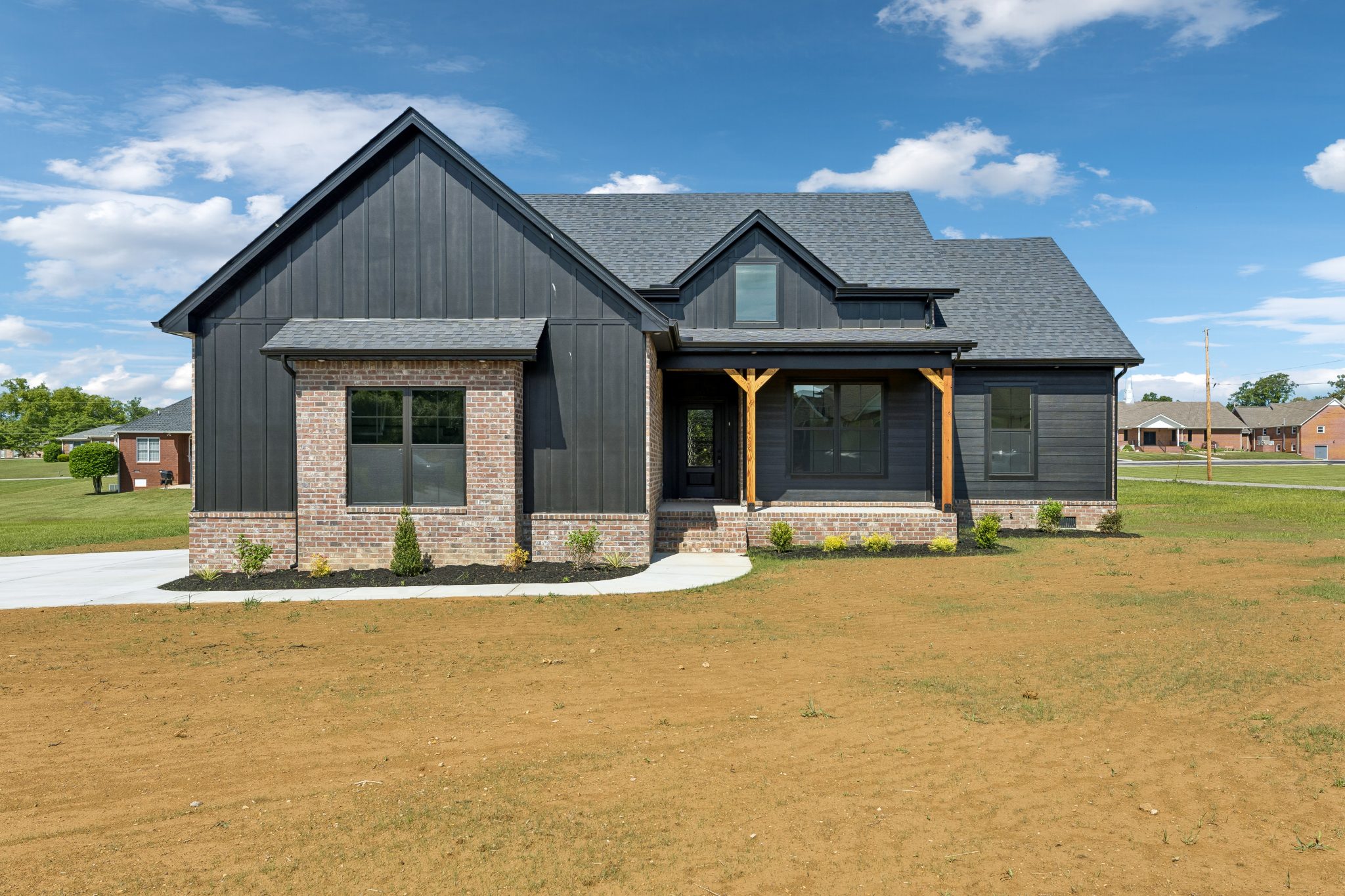 Modern black and brick house with gable roof in suburban setting, clear blue sky.