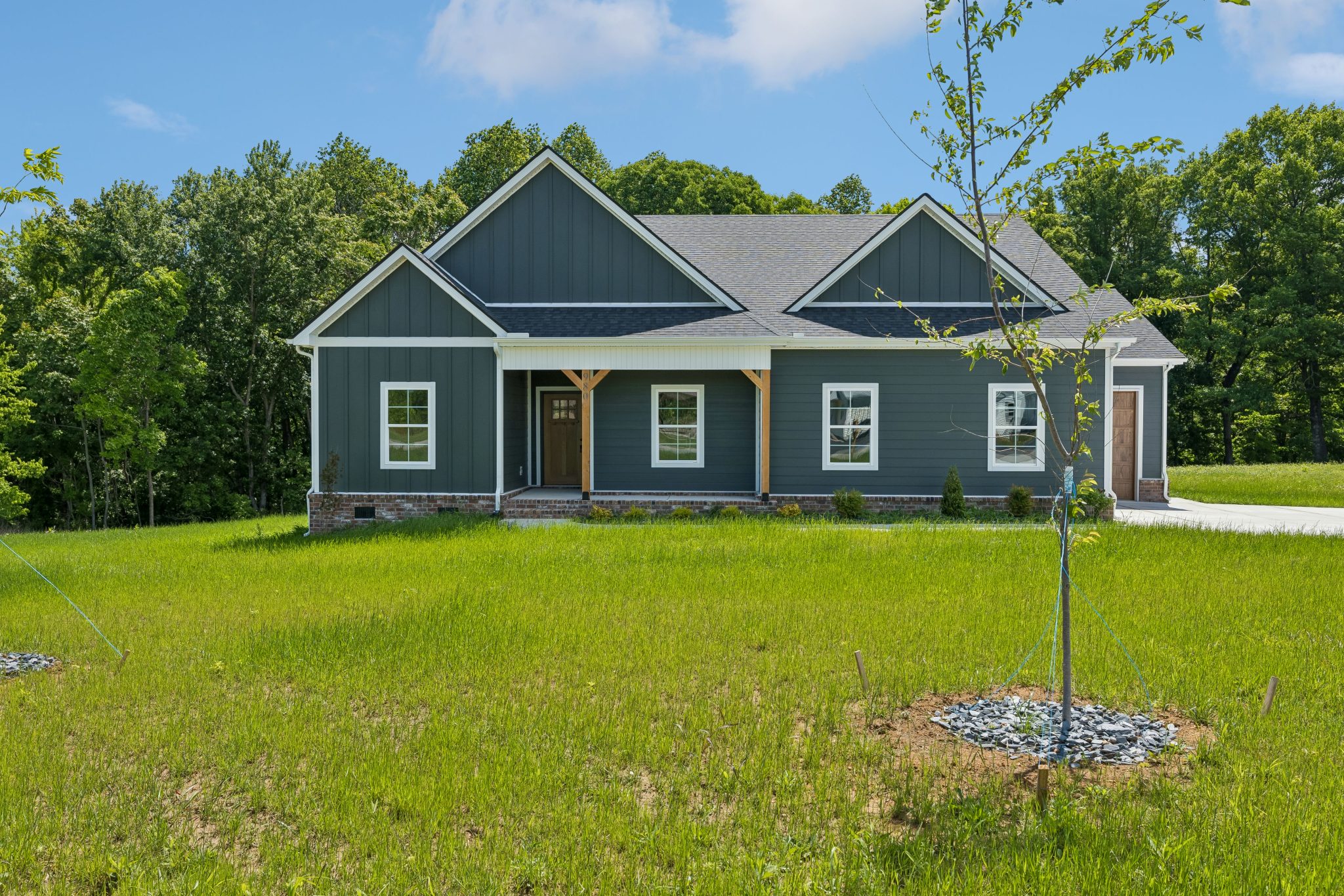Modern single-story house with dark siding and lush green lawn in a serene wooded setting.