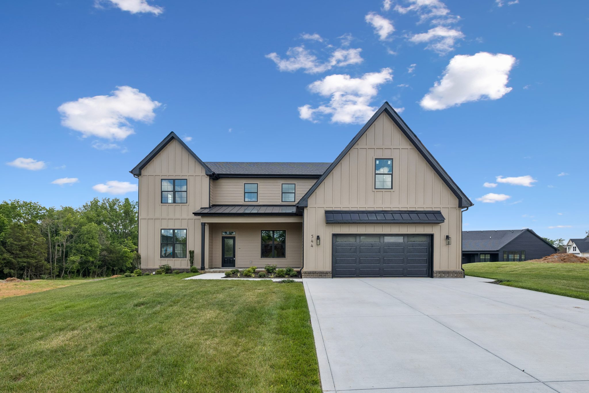 Modern two-story home with gabled roof, spacious lawn, and blue sky background.