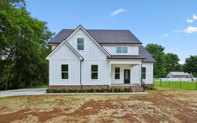 Modern white house with black roof and large windows, surrounded by greenery and blue sky.