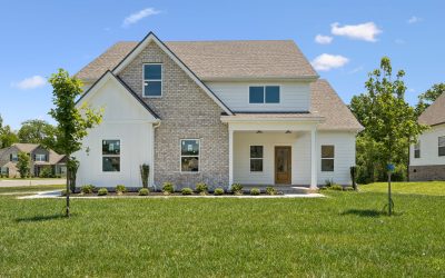 Modern suburban home with brick and siding exterior, front lawn, and trees under a blue sky.