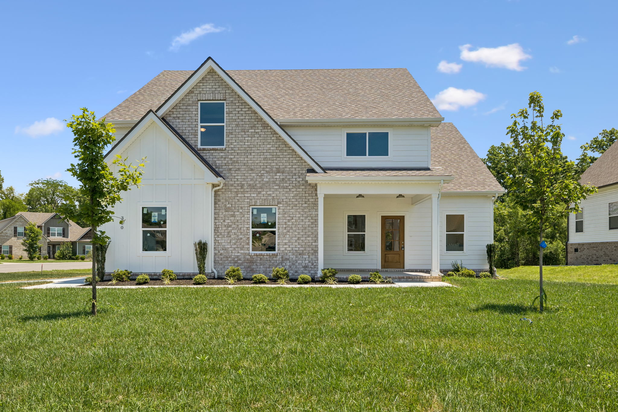 Modern suburban home with brick and siding exterior, front lawn, and trees under a blue sky.