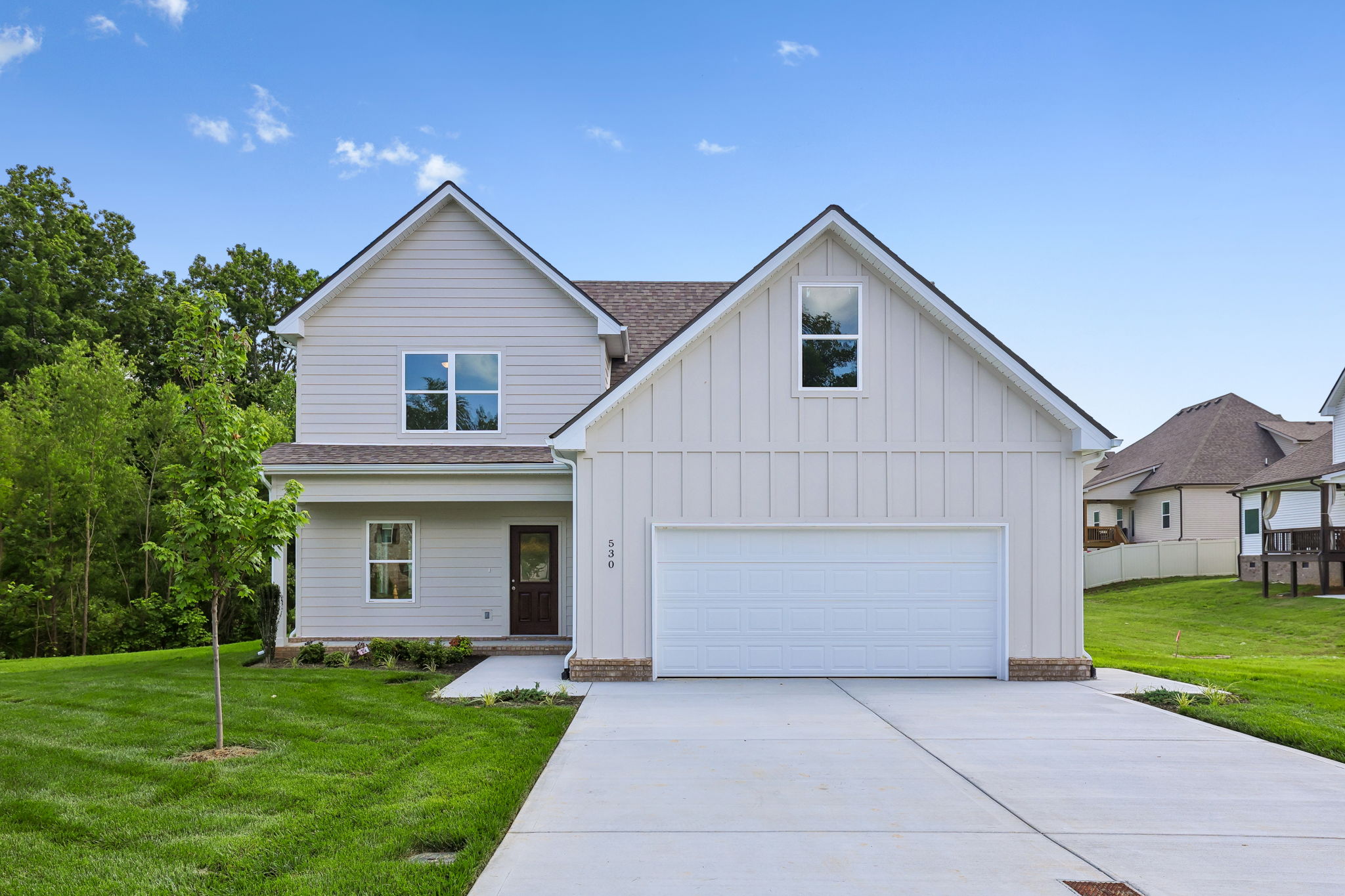 Modern suburban house with two-car garage and manicured lawn under clear blue sky.