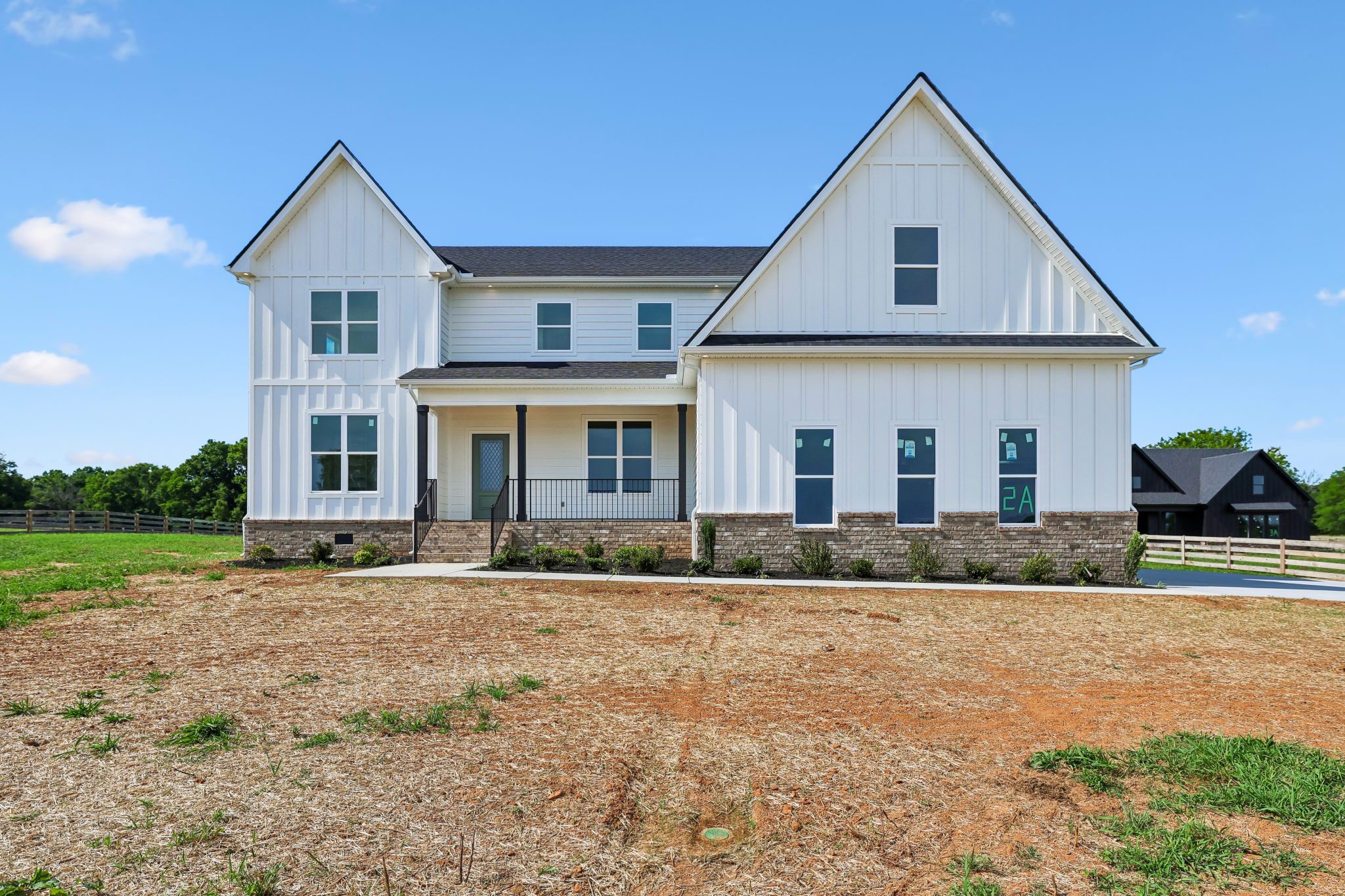 Front view of a white modern farmhouse with brick accents and a large front yard.
