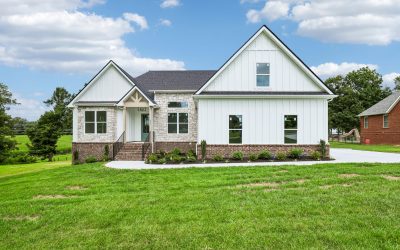 Modern white farmhouse with brick accents, green lawn, and blue sky.