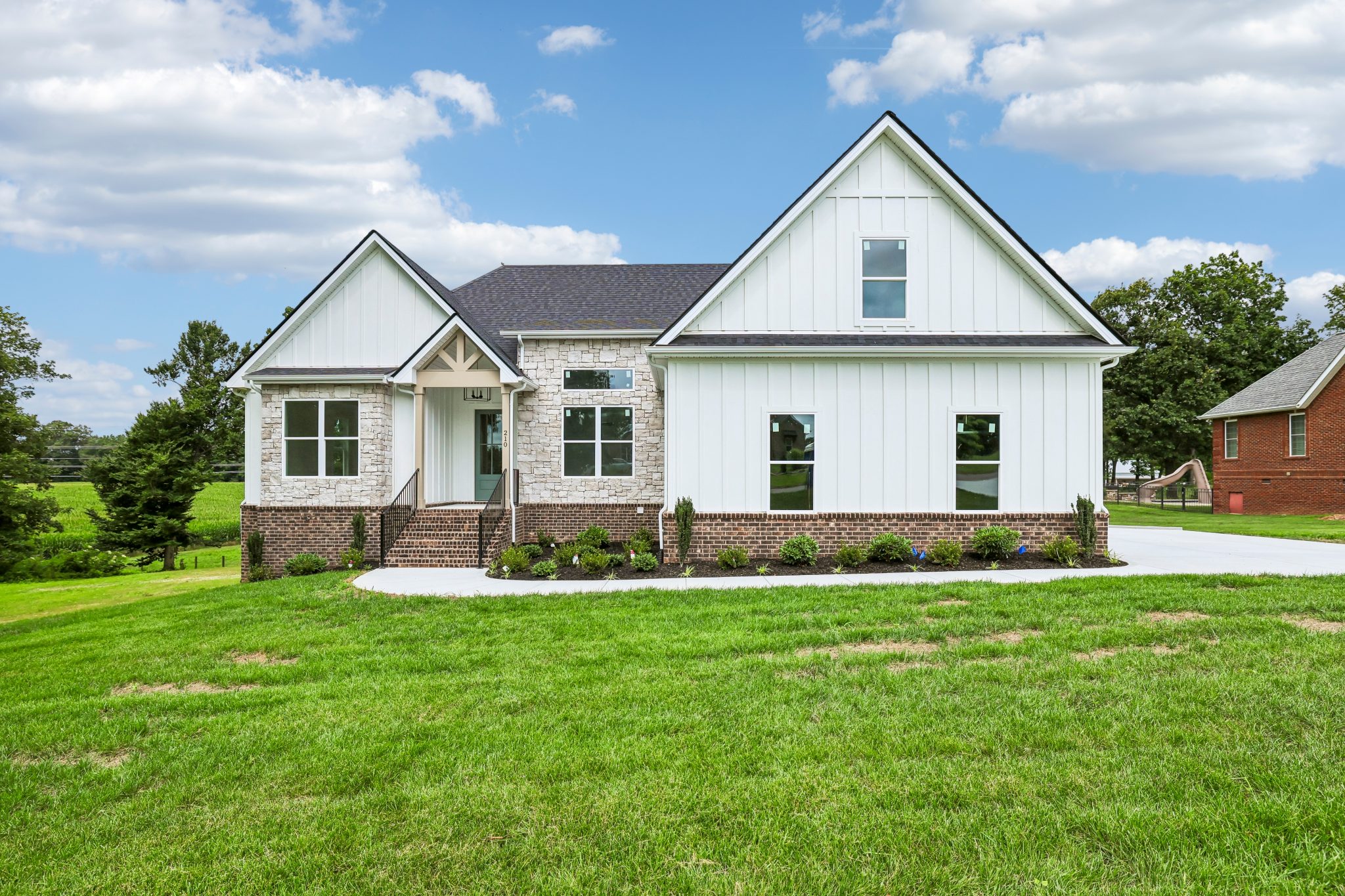 Modern white farmhouse with brick accents, green lawn, and blue sky.