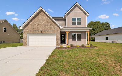 Modern suburban house with brick facade, wide driveway, and green lawn under a clear blue sky.