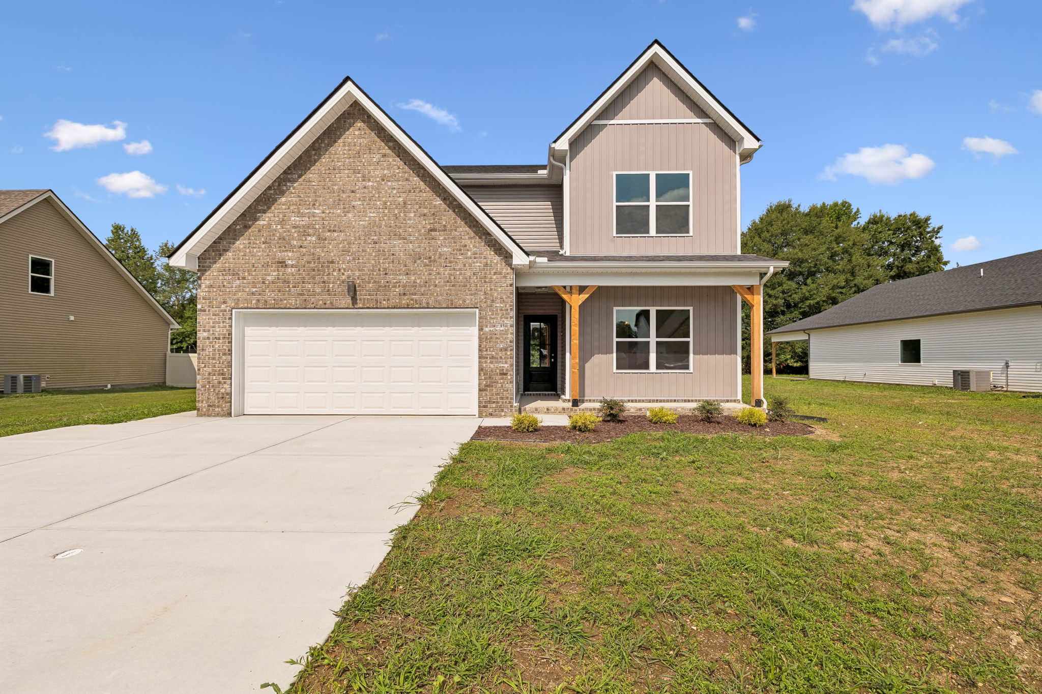 Modern suburban house with brick facade, wide driveway, and green lawn under a clear blue sky.