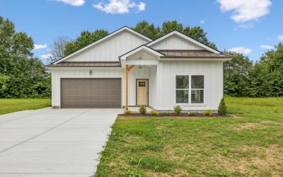 Modern white house with gray garage, lush green lawn, and clear blue sky background.