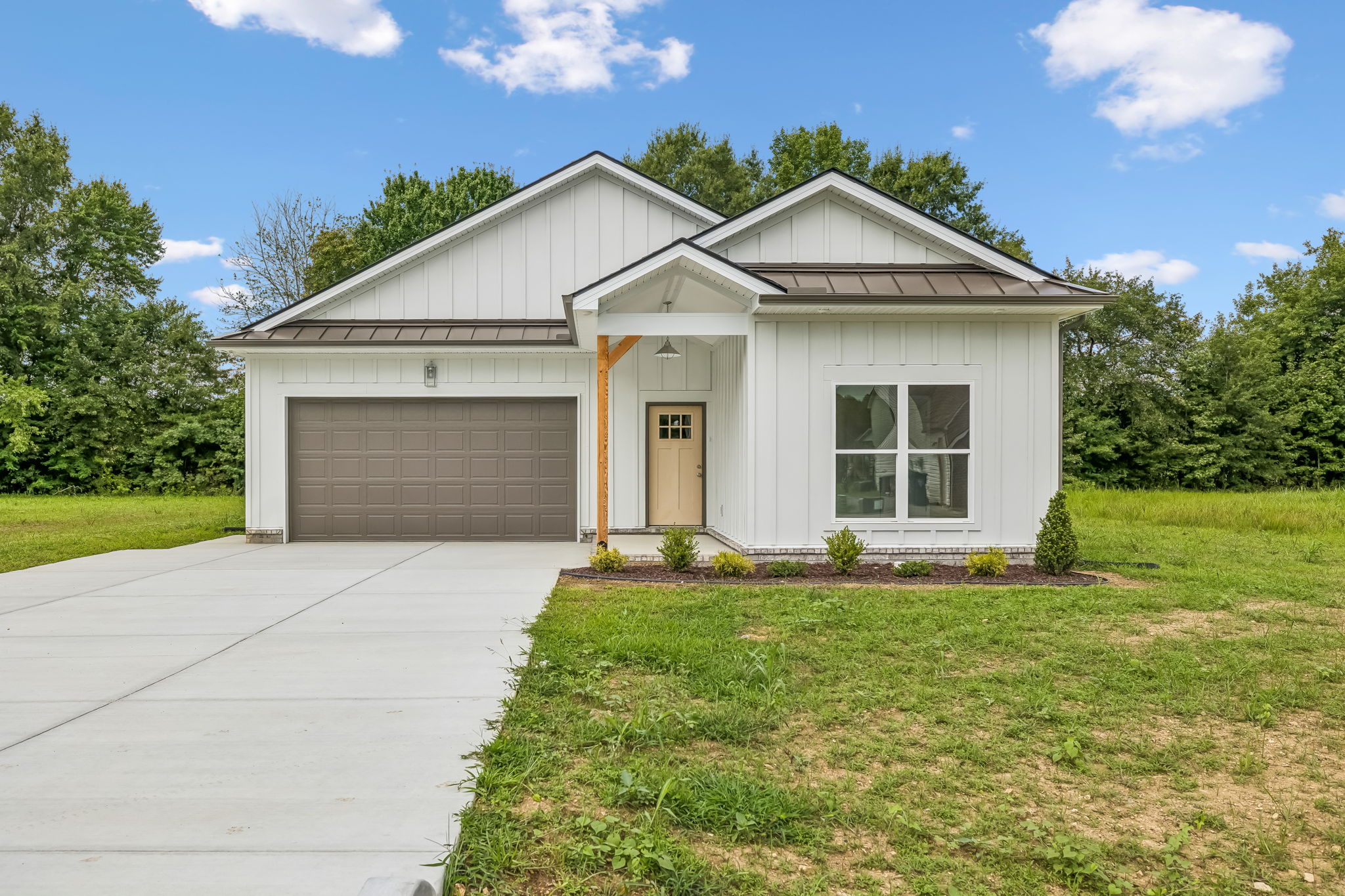 Modern white house with gray garage, lush green lawn, and clear blue sky background.