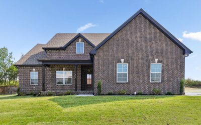 Brick house with gabled roof and front lawn under a clear blue sky.