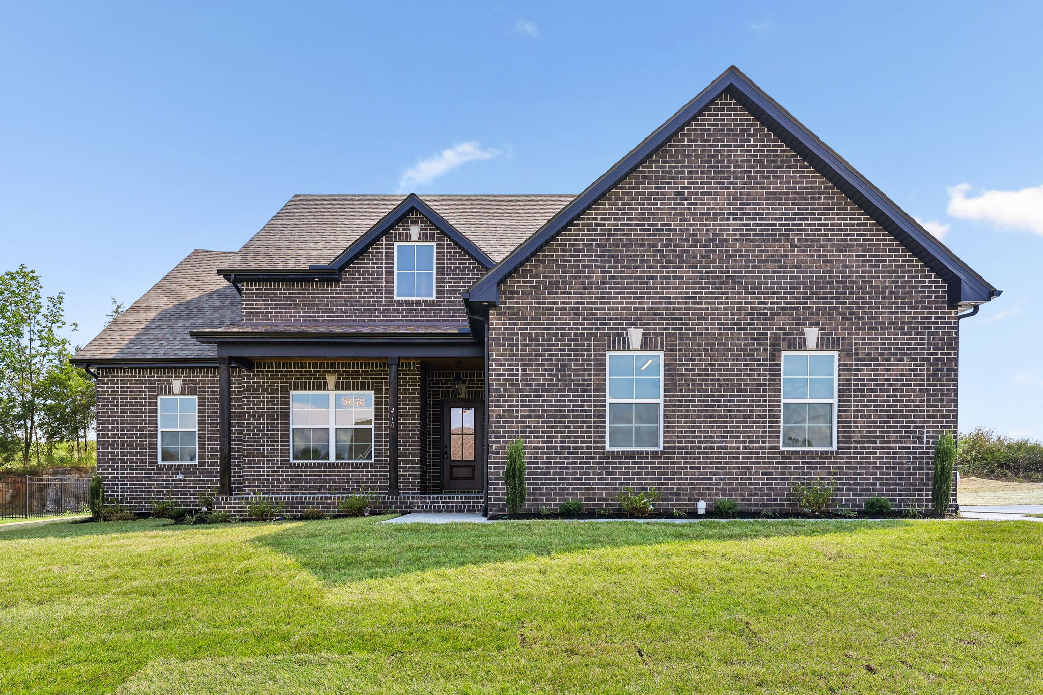 Brick house with gabled roof and front lawn under a clear blue sky.