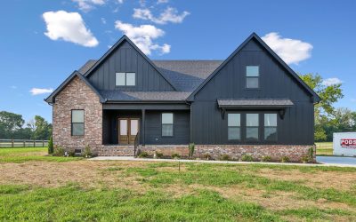 Modern black and brick house with gable roof and green lawn under blue sky.