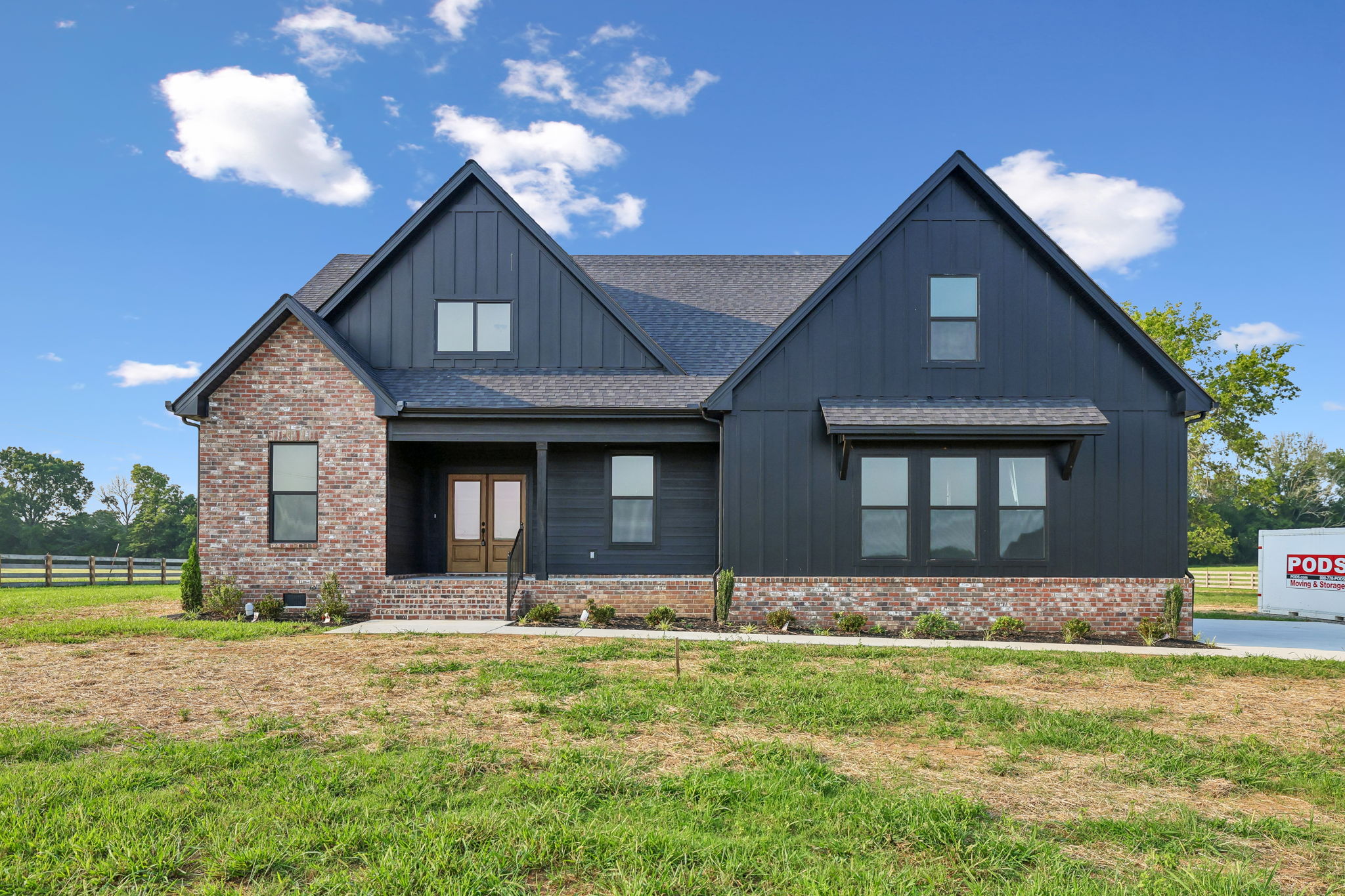 Modern black and brick house with gable roof and green lawn under blue sky.