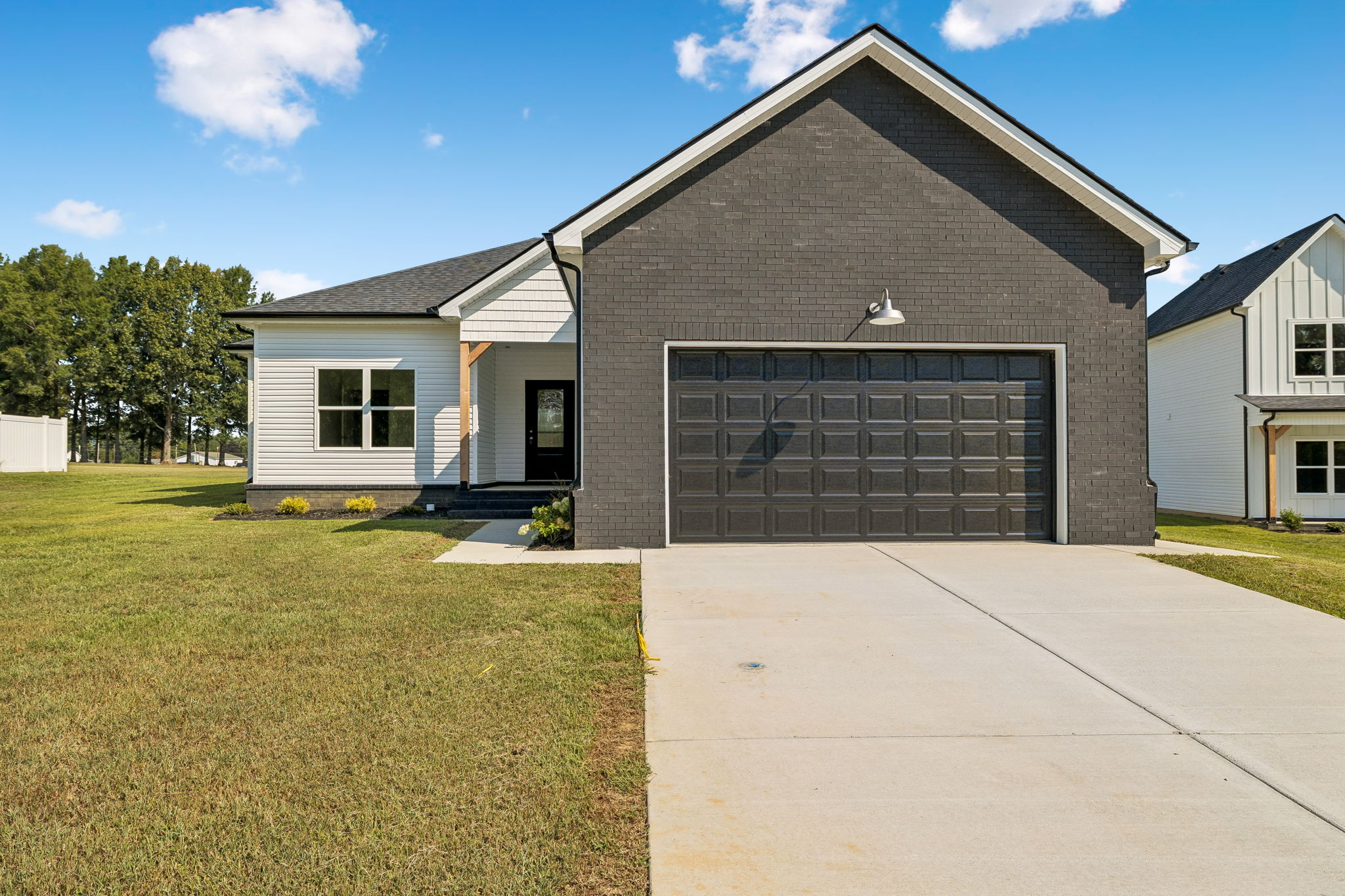 Modern single-story house with black brick facade and white siding, spacious driveway.